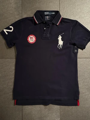 Ralph Lauren Team USA Olympics London - Marinblå (Herr M) - Säljer en riktigt unik limiterad edition Ralph Lauren pikétröja från OS i London 2012. Tröjan är gjord som en del av Ralph Laurens officiella Team USA-kollektion och är svår att hitta idag. Tröjan är i ganska bra skick men har någon mindre fläck (se bild)
