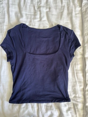Mörkblå topp med fyrkantig ringning - En stilren mörkblå topp med korta ärmar och fyrkantig ringning. Perfekt att matcha med jeans eller kjol för en enkel och snygg look. Tillverkad i mjukt material som känns skönt mot huden.