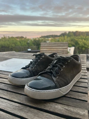 Gröna Lanvin sneakers med lackad tå - Snygga gröna sneakers från Lanvin med svart lackad tå och vita sulor. Skorna har klassisk snörning och en stilren design som passar till många outfits. Materialmix av mocka och lack ger en lyxig känsla. Perfekta för dig som gillar exklusiva sneakers.