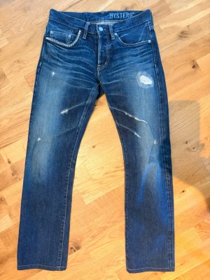 Hysteric Glamour jeans - Snygga blå jeans från Hysteric med slitna detaljer och patch på låret. Slimfit femficksmodell med snygg tvätt. •Midja: 38,5cm •Längd: 98cm               •Innersöm: 71,5 cm • Ben öppning: 18,5cm