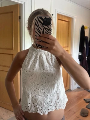 Vit broderad ärmlös linnetopp - Superfin vit ärmlös linnetopp med broderade detaljer och hålmönster ifrån missay i storlek M, men skulle säga att det mer är en xs. Toppen har hög hals och en lätt utsvängd passform med vågig kant nertill. Perfekt för varma dagar och ger en fräsch och somrig look. Har lite sminkfläckar vid kragen som borde gå lätt bort i tvätten. 