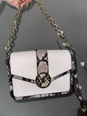 Vit Michael Kors handväska med kedja - Snygg vit handväska från Michael Kors med detaljer i ormskinnsmönster och guldfärgad kedja. Väskan har ett stort MK-emblem framtill och stilren, rektangulär form. Perfekt accessoar för att lyfta din outfit. Väskan är som ny använd sparsam som max 2-3 gånger. 