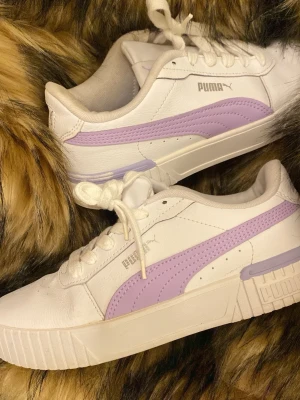 Vita och lila sneakers från Puma - MÖTS UPP I STOCKHOLM ‼️‼️Snygga vita sneakers från Puma med lila detaljer längs sidan och vid hälen. Skorna har klassisk låg modell, vita snören och är tillverkade i slätt syntetmaterial. Perfekta för en trendig och sportig look.