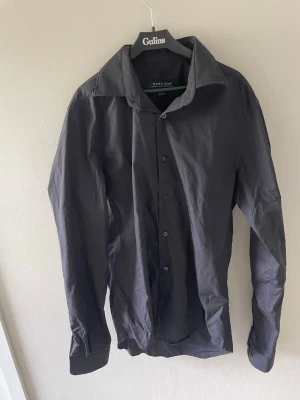 Svart skjorta från Zara Man - Klassisk svart skjorta från Zara Man med lång ärm och knappar framtill. Skjortan har en stilren design med bred krage och är tillverkad i ett lätt och bekvämt material, perfekt för en clean och enkel look.