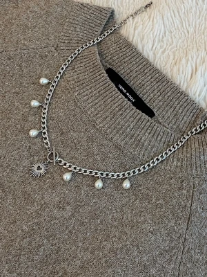 Silverfärgat halsband med pärlor - Stilrent halsband i silverfärgad rostfritt med kedja, dekorerat med droppformade pärlor och ett solformat hänge. Perfekt för att ge din outfit en trendig touch. Passar till många olika stilar och är lätt att matcha med andra smycken.