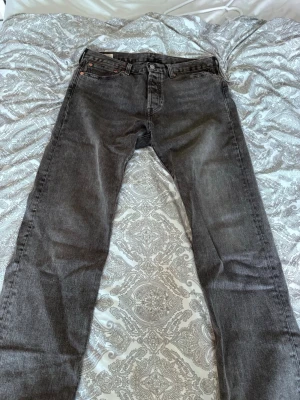 501 Jeans från Levi's 32/32 - Säljer ett par svarta jeans från Levi's med klassisk rak passform. Jeansen har fem fickor, knappgylf och Levi's ikoniska läderpatch bak i midjan. Perfekta till en avslappnad stil och funkar året runt.