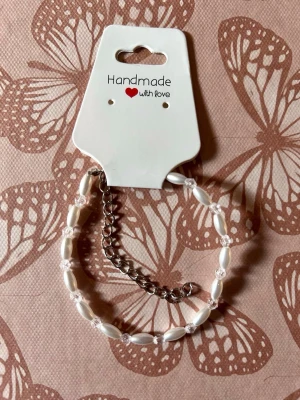 Handgjort pärlarmband med kedja - Ett stilrent handgjort armband med vita avlånga pärlor och små genomskinliga pärlor, ihopkopplat med en silverfärgad kedja. Perfekt accessoar för att lyfta din outfit med en personlig touch.
