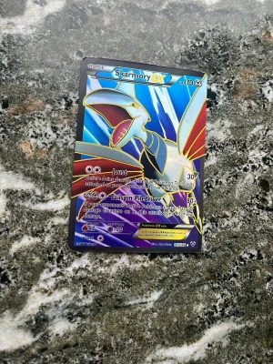 Pokémonkort Skarmory EX holografisk - Säljer ett Pokémonkort av Skarmory EX med holografisk yta. Kortet har färger i blått, rött, gult och silver med coolt motiv och detaljerad design. Perfekt för samlare eller Pokémonfans som vill utöka sin kortsamling.