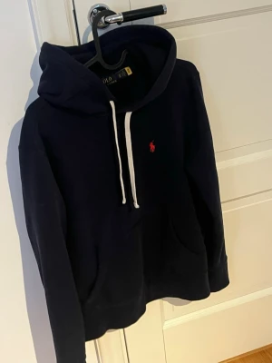 Polo Ralph Lauren hoodie - Mörkblå hoodie från Polo Ralph Lauren med vit dragsko och klassisk röd logga broderad på bröstet. I storlek XS