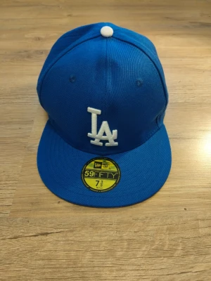 Blå LA Dodgers keps New Era 59FIFTY - Snygg blå keps från New Era 59FIFTY med LA Dodgers-logga broderad i vitt framtill. Klassisk flat peak och grå undersida på skärmen. Perfekt för dig som gillar streetwear och sportiga accessoarer.