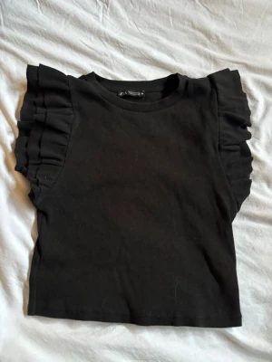 Svart Topp från Zara - Snygg svart topp från Zara med volangdetaljer. Modellen är croppad och har rund halsringning. skriv för fler frågor/ bilder 💕