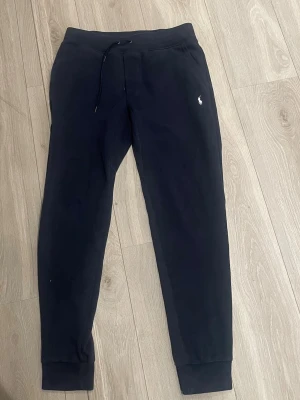 Svarta mjukisbyxor från Polo Ralph Lauren - Snygga svarta mjukisbyxor från Polo Ralph Lauren med dragsnöre i midjan och ribbade muddar vid benslut. Diskret logga broderad på framsidan och en bakficka. Perfekta för chill eller träning.
