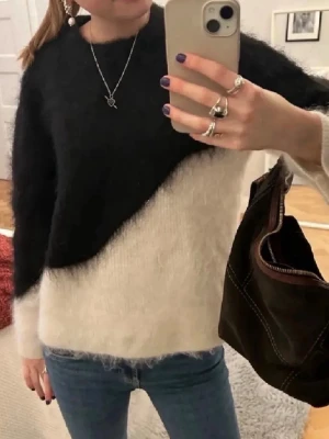 Svartvit fluffig stickad tröja - Säljer en snygg stickad tröja i svart och vitt med diagonal färgdelning. Tröjan är fluffig och har en avslappnad passform med långa ärmar. Perfekt för dig som gillar en trendig och mysig look.