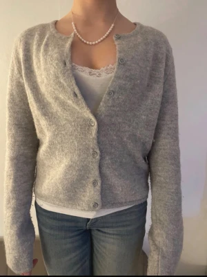 Ljusgrå kofta från Gina Tricot - Mysig ljusgrå kofta från Gina Tricot i fluffigt material. Koftan har rund halsringning, knappar framtill och långa ärmar. Enkel och stilren design som passar perfekt till jeans eller kjol.