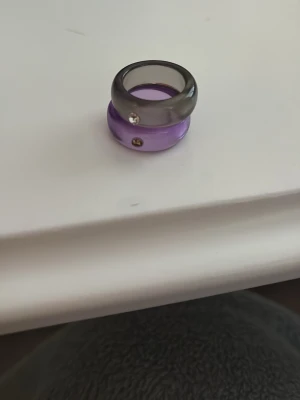 Två chunky ringar i plast/akryl - Säljer två chunky ringar i akryl, en i lila och en i grått. Båda ringarna har en liten infattad sten framtill som ger extra bling. Perfekta för att ge din look en färgklick och trendig känsla. I storlek 16 eller 17 jag vet inte riktigt. Osäker vart den är ifrån men kan vara från hm, gina tricot eller Kappahl 