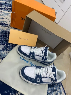 Louis Vuitton  sneakers - Snygga Louis Vuitton sneakers i blått och vitt med klassiskt monogrammönster på denimdetaljer. Skorna har vita snören, vit sula och en cool kontrast mellan tyg och läder. Perfekta för dig som vill sticka ut med exklusiv streetstyle.