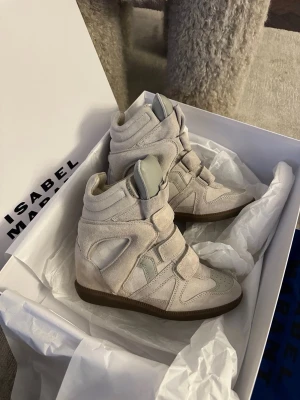 Beige Isabel Marant - Snygga höga sneakers från Isabel Marant i beige mocka med detaljer i lä sop och kardborreband. Skorna har en chunky sula och ikonisk design som ger en cool och trendig look. Perfekta för dig som vill sticka ut med stilrena och unika sneakers.