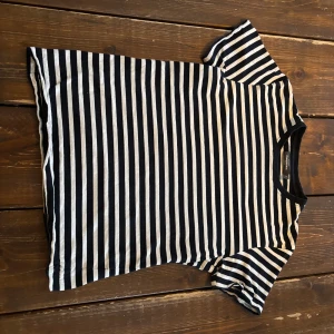 Randig t-shirt i bomull från Monki - Säljer en klassisk randig t-shirt från Dressman i svart och vit. T-shirten har korta ärmar, rund halsringning och är gjord i mjuk bomull. Perfekt till jeans eller kjol för en enkel och stilren look.