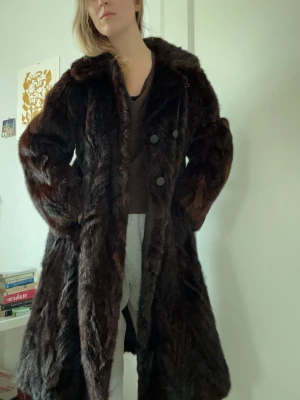 Mörkbrun lång pälsjacka - Säljer en lång, mörkbrun pälsjacka med dubbelknäppning framtill och bred krage. Jackan har en klassisk, rak passform. Vintage. Frakt tillkommer 
