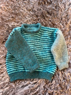 Randig stickad tröja i blå toner - Tröjan är stickad i fem trådar Mohair och merinoull (muliseringsfri merinoull). Kostnaden för materialet vill jag inte ens tänka på, dyyyrt.  Hoppas att denna härliga tröja skall hålla någon härlig unge varm.