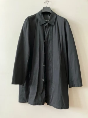 Svart klassisk rock med knappar - Stilren svart rock med rak passform och knäppning framtill. Rocken har klassisk krage och långa ärmar, perfekt för en minimalistisk look. Tillverkad i ett slätt tyg som ger en snygg siluett.