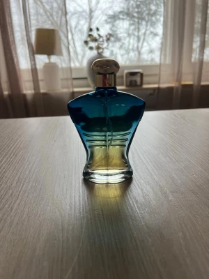 Jean Paul Gaultier Le Male parfym - Säljer en ikonisk parfym från Jean Paul Gaultier, Le Male. Flaskan har en unik form som en manlig torso och är gjord av glas med en gradient från blått till gult. Den har en silverfärgad kork och är perfekt för dig som vill ha en klassisk och stilren doft.