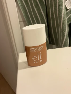 e.l.f. Bronzing Drops Rose Gold - Bronzing drops från e.l.f. i nyansen Rose Gold. Kommer i en smidig plastflaska med vit kork. Ger huden en solkysst glow och innehåller antioxidanter samt solrosfröolja för extra näring. Perfekt för att boosta din basrutin med en fräsch bronzig finish. Ej använd.