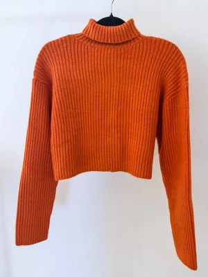 Orange stickad polotröja från H&M - Trendig orange ribbstickad polotröja från H&M. Croppad modell med långa ärmar och hög krage. Perfekt för att addera färg till din outfit. Tillverkad i mjukt stickat material som känns skönt mot huden.