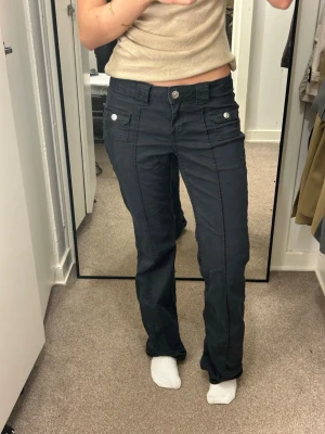 Svarta cargobyxor med fickor - Snygga svarta cargo  jeans  från H&M med låg midja och lätt bootcut/flare nertill 👖 Supertrendiga och ger den perfekta y2k-siluetten. Fickdetaljer framtill och markerade sömmar som gör dem extra unika 🤍  Sitter tajt över höfter och lår men faller snyggt över skorna – perfekta till klackar eller sneakers. Matcha med en tight topp för en it-girl look eller oversized tröja för mer casual vibe.