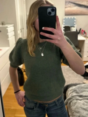 Grön stickad topp med puffärm - Säljer en grön stickad topp med korta puffärmar och rund hals. Tröjans passform ger en trendig look. Perfekt att matcha med jeans eller kjol för en mer uppklädd outfit.