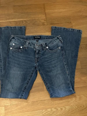 True Religion jeans - NELLY ULTRA LOW RISE JOEY FLARE SN Ultra low waist flared jeans från Nelly med dekorativa rosa sömmar. Köpta från Nelly för 1399kr som är i mycket bra skick använda endast en gång. Storlek W27 Pris kan diskuteras