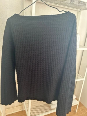 Svart ribbstickad tröja XS från 157 - Svart ribbstickad tröja från 157 i storlek XS. Tröjan har lång ärm, rund halsringning och ett diskret vågigt avslut vid ärmslut och nederkant. Materialet är mjukt och stretchigt, perfekt för lager på lager eller som den är.