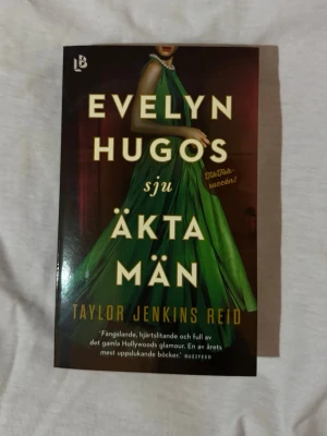 Evelyn Hugos sju äkta män - Säljer boken 'Evelyn Hugos sju äkta män' av Taylor Jenkins Reid. Omslaget är mörkt med en kvinna i en grön klänning och tydlig gul text. Boken är en pocketutgåva och handlar om Hollywoods glamour och hemligheter. Perfekt för dig som gillar dramatik och kärlek.