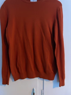 Rostbrun stickad tröja - En enkel och stilren rostbrun stickad tröja med rund halsringning och långa ärmar. Tröjan har ribbade muddar vid ärmslut och nederkant. Perfekt för lager på lager och passar till det mesta i garderoben.