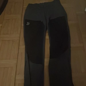 Svarta byxor från Haglöfs - Snygga svarta byxor från Haglöfs med förstärkta partier på knäna och logga på låret. Perfekta för dig som gillar en sportig och funktionell stil. Byxorna har rak passform och elastisk midja för extra komfort.