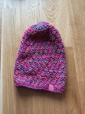 Färgglad virkad mössa från Selfie Zone - Säljer en virkad mössa från Selfie Zone i starka färger som rosa, orange och blå. Mössan har en avslappnad passform och är tillverkad i ett mjukt garn som känns skönt mot huvudet. Perfekt för dig som vill sticka ut med en unik accessoar.