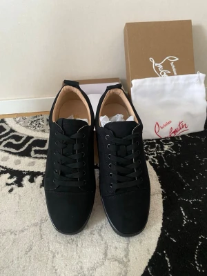 Svarta sneakers från Christian Louboutin - Stilrena svarta sneakers från Christian Louboutin med lågt skaft och svarta skosnören. Skorna har en ovandel i mocka och insida i ljust läder. Klassisk design med diskreta detaljer och ikonisk röd logga på förpackningen.