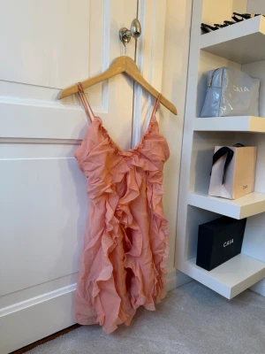 Rosa volangklänning med smala band - Supersöt rosa kortklänning med tunna axelband och massor av volanger framtill. Klänningen har en lätt och luftig känsla, perfekt för varma dagar. Dragkedja i ryggen för enkel påklädning. Ingen synlig logga eller märke. Använd 1 gång! Så himla snygg till sommaren / semester