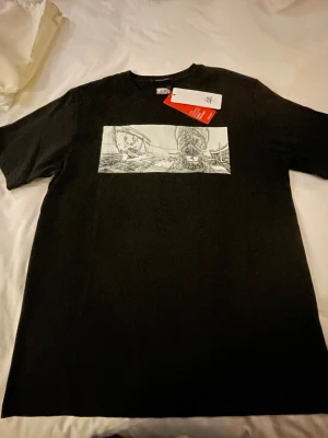 Svart t-shirt från C.P. Company - Svart t-shirt från C.P. Company med ett grafiskt tryck i vitt på framsidan och vit text på ryggen. Klassisk passform och rund halsringning. Perfekt för dig som gillar streetwear och stilrena detaljer.