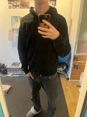 Svart zip hoodie från H&M - Säljer en klassisk svart hoodie från H&M med dragkedja framtill och två fickor. Hoodien har justerbar huva med snören och ribbade muddar vid ärmar och nederkant. Perfekt för en avslappnad och stilren look.