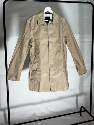 Beige rock J.Lindeberg - Sick 10/10 Helt ny saknar endast etiketter.         Stilren beige rock med enkel knäppning framtill och två sidofickor. Rocken har en rak passform, klassisk krage och dekorativa knappar vid ärmsluten. Perfekt till vår och höst.