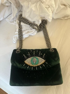 Mörkgrön sammetsväska från Kurt geiger  - Unik mörkgrön handväska i sammet med grov silverfärgad kedjerem och ett broderat öga i pärlor och paljetter på locket.