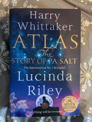 Atlas: The Story of Pa Salt - Säljer boken 'Atlas: The Story of Pa Salt' av Lucinda Riley och Harry Whittaker. Omslaget är blått med stjärnhimmel och guldtext, och boken är på engelska. Det är den sista delen i Seven Sisters-serien och bjuder på en episk avslutning med magisk och gripande berättelse.
