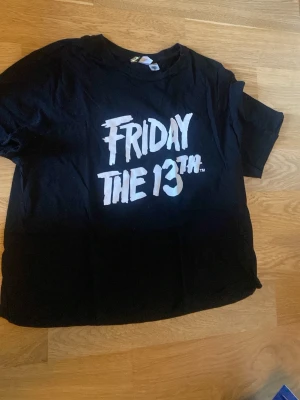 Svart Friday the 13th t-shirt - Cool svart t-shirt med trycket 'Friday the 13th' i vitt framtill. Perfekt för dig som gillar skräckfilmer och vill ha en statement-tee i garderoben. Klassisk passform och rund halsringning.