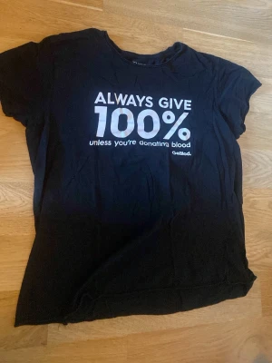 Svart t-shirt med texttryck - Cool svart t-shirt med vitt texttryck på bröstet där det står 'ALWAYS GIVE 100% unless you're donating blood'. Klassisk passform och rund hals. Perfekt för dig som gillar statement-plagg.