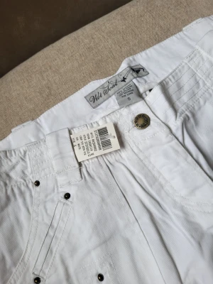 Vita cargo shorts från Wet Seal storlek US5 M - Vita cargo shorts från Wet Seal med flera fickor, dekorativa nitar och snörning vid bensluten. Tillverkade i bomull för en skön och luftig känsla. Perfekta för varma dagar och en avslappnad stil.