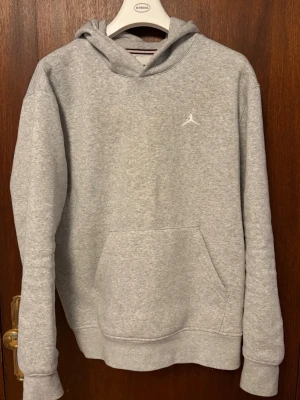 Grå Jordan hoodie - Snygg grå hoodie från Jordan med klassisk huva och känguruficka framtill. Diskret Jumpman-logga broderad på bröstet. Tillverkad i mjukt bomullsmaterial som känns skönt mot huden. Perfekt för en avslappnad och sportig stil.