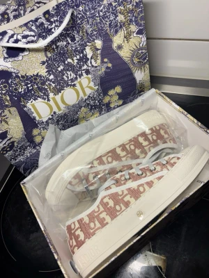 walk n dior platform sneaker - Snygga sneakers från Dior med rosa och vit monogramdesign. Skorna har vita snören, gummisula med stjärndetalj undertill och tydlig Christian Dior-logga på sidan. Ovandelen är i textil och sulan är i kraftigt vitt gummi. Perfekta för dig som vill sticka ut med lyxig streetstyle.