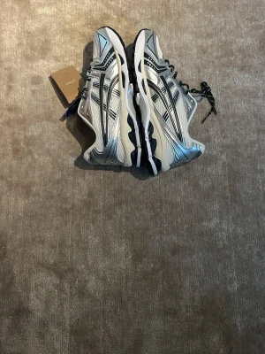 Asics silver och svarta sneakers - Snygga sneakers från Asics i silver och svart med coola detaljer och sportig design. Skorna har en chunky vit sula och klassiska Asics-stripes på sidorna. Ovandelen är i mesh och syntetmaterial för bra andningsförmåga och komfort. Perfekta för dig som gillar streetwear. Pris kan diskuteras vid snabb affär