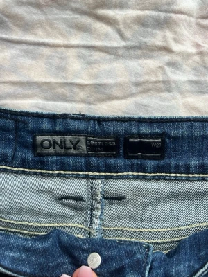 Blå denimshorts från ONLY - Säljer ett par klassiska blå denimshorts från ONLY med snygga kontrastsömmar och två bakfickor. Shortsen har normal passform och är perfekta för varma dagar. Tillverkade i slitstark bomull med en tidlös look.